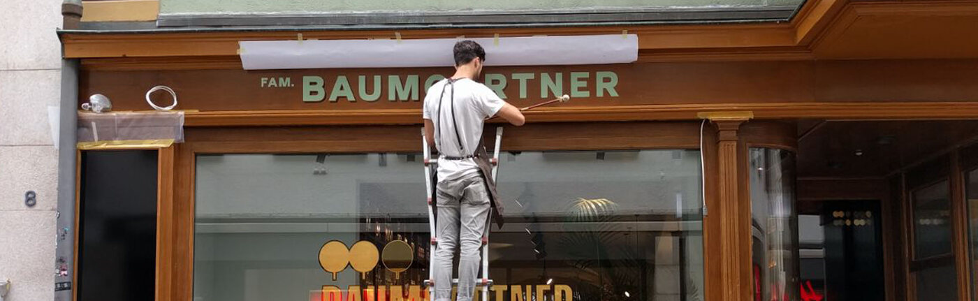 Patrick Baumgartner - Artist painting family name on a shop wall